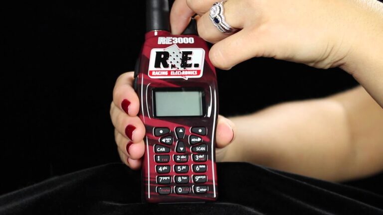 A person holding a R.E. 3000 Racing Electronics scanner with red casing and an antenna, set against a black background.